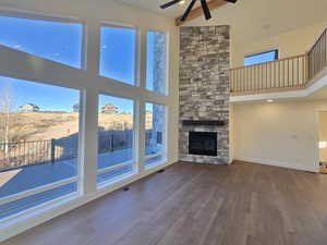 Unfurnished living room featuring a towering ceiling, plenty of natural light, dark wood-style flooring, a stone fireplace, and ceiling fan