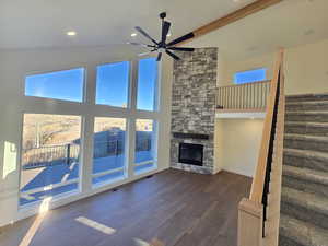 Unfurnished living room featuring a towering ceiling, a ceiling fan, a fireplace, dark wood-type flooring, and stairs