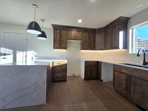 Kitchen with dark brown cabinetry, pendant lighting, dark wood-style floors, light stone counters, and recessed lighting
