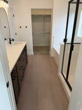 Full bathroom featuring double vanity, a walk in closet, a stall shower, a bath, and light wood finished floors