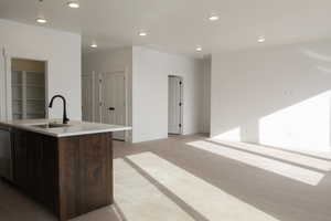 Kitchen featuring recessed lighting, an island with sink, dark wood finish cabinetry, dishwasher, and light stone counters