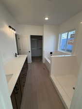 Bathroom with double vanity, a bath, a spacious closet, and light wood-style flooring