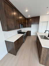 Kitchen featuring dark brown cabinets, tasteful backsplash, gas stove, light wood-type flooring, and recessed lighting