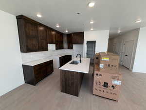 Kitchen featuring dark brown cabinetry, decorative backsplash, a center island with sink, light wood-style flooring, and recessed lighting