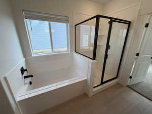 Bathroom with a stall shower, healthy amount of natural light, a garden tub, and wood finished floors