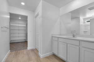 Bathroom featuring a walk in closet, vanity, light wood-style flooring, recessed lighting, and a shower