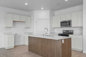 Kitchen featuring gas range, white cabinetry, light wood finished floors, a center island with sink, and stainless steel microwave