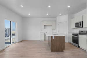 Kitchen with appliances with stainless steel finishes, light wood-type flooring, recessed lighting, an island with sink, and white cabinetry