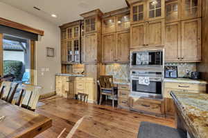 Kitchen featuring oven, glass insert cabinets, light stone counters, black microwave, and backsplash