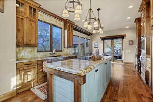 Kitchen with light stone countertops, a center island, decorative backsplash, glass insert cabinets, and decorative light fixtures