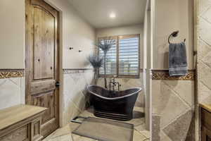 Full bath with a wainscoted wall, a soaking tub, and tile walls