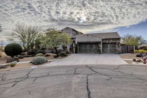 View of front of house featuring a garage, concrete driveway, stone siding, and a tile roof
