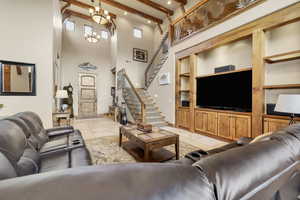 Living room featuring built in features, light tile patterned flooring, beamed ceiling, a high ceiling, and stairs