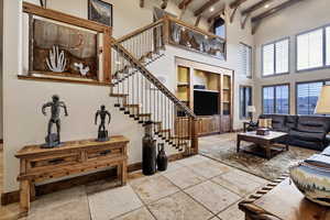 Living area with a towering ceiling, beamed ceiling, stone tile floors, built in shelves, and stairs