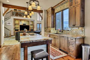 Kitchen with light stone countertops, decorative light fixtures, a center island, brown cabinets, and beam ceiling