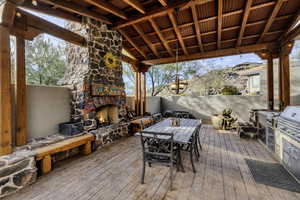 Wooden deck with outdoor dining area, area for grilling, and an outdoor stone fireplace
