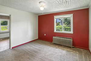 Empty room with radiator heating unit, carpet, radiator, a textured ceiling, and ornamental molding