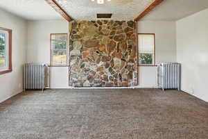 Carpeted spare room featuring radiator, a textured ceiling, beamed ceiling, and healthy amount of natural light