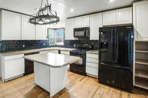 Kitchen featuring black appliances, white cabinets, a center island, a textured ceiling, and hanging light fixtures
