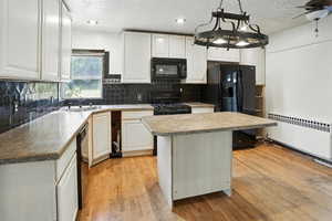 Kitchen with a center island, radiator heating unit, a textured ceiling, white cabinetry, and black appliances