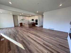 Kitchen with open floor plan, recessed lighting, a kitchen island with sink, white cabinetry, and dark wood-style flooring