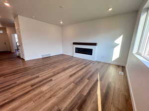Unfurnished living room with plenty of natural light, recessed lighting, dark wood-type flooring, and a glass covered fireplace