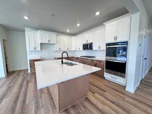Kitchen with white cabinetry, recessed lighting, stainless steel appliances, light stone countertops, and an island with sink