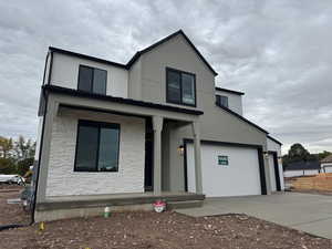 View of front facade featuring stone siding, covered porch, concrete driveway, and an attached garage
