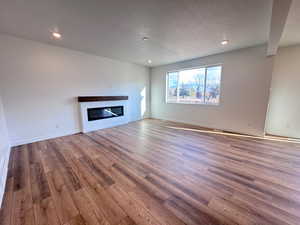 Unfurnished living room featuring recessed lighting, a glass covered fireplace, light wood-style floors, and a textured ceiling