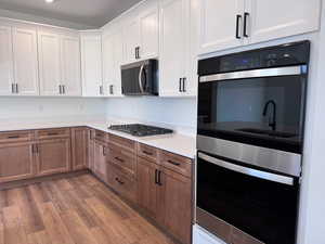 Kitchen featuring stainless steel appliances, white cabinetry, light wood finished floors, brown cabinetry, and light stone countertops