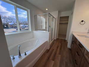 Bathroom featuring a walk in closet, vanity, dark wood-style floors, a stall shower, and a garden tub