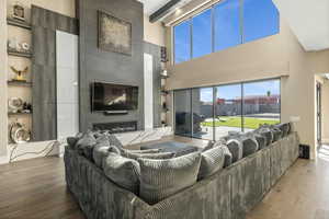 Living area with a premium fireplace, hardwood / wood-style floors, a high ceiling, beamed ceiling, and built in shelves