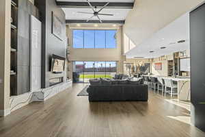 Living room with hardwood / wood-style flooring, ceiling fan, a fireplace, a high ceiling, and recessed lighting