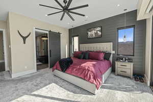 Carpeted bedroom featuring a barn door connected bathroom, a ceiling fan, and an accent wall