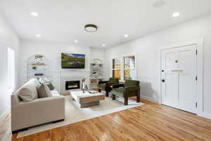 Living room featuring built in features, a fireplace, light wood-style flooring, and recessed lighting