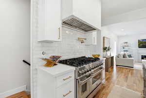 Kitchen with range with two ovens, wood floors, tasteful backsplash, and white cabinetry