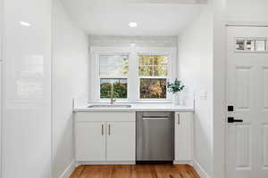 Kitchen featuring white cabinets, dishwasher, wood flooring, and light stone countertops