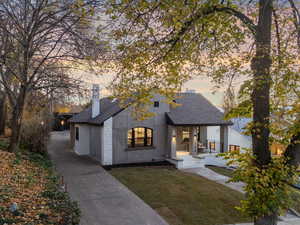 View of front of house with roof with shingles, a front yard, a chimney, and stucco siding