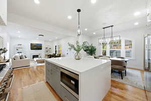 Kitchen with hanging light fixtures, built in appliances, a glass covered fireplace, a center island, and wood flooring