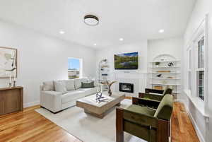 Living area featuring a glass covered fireplace, wood floors, built in features, and recessed lighting