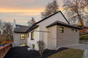 Property exterior at dusk with a shingled roof, a chimney, and stucco siding