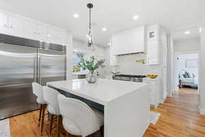 Kitchen with a kitchen bar, built in fridge, white cabinets, a center island, and recessed lighting