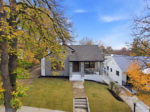 View of front facade featuring covered porch, roof with shingles, a front yard, and stucco siding