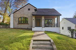 Contemporary home featuring a shingled roof, a front lawn, covered porch, and stucco siding