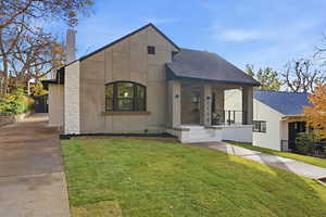 Contemporary home with a shingled roof, a front lawn, stucco siding, a chimney, and covered porch