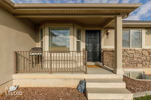 Doorway to property featuring stucco siding, stone siding, and a porch
