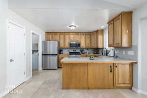 Kitchen with light countertops, a peninsula, brown cabinets, stainless steel appliances, and washer / dryer