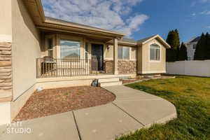 View of exterior entry featuring stucco siding, a porch, a shingled roof, and stone siding