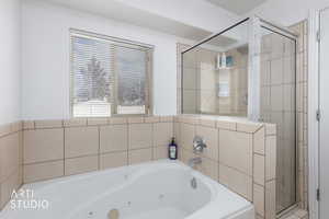 Bathroom with a tub with jets, healthy amount of natural light, and a stall shower