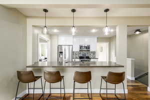 Kitchen featuring dark countertops, a peninsula, appliances with stainless steel finishes, tasteful backsplash, and white cabinetry